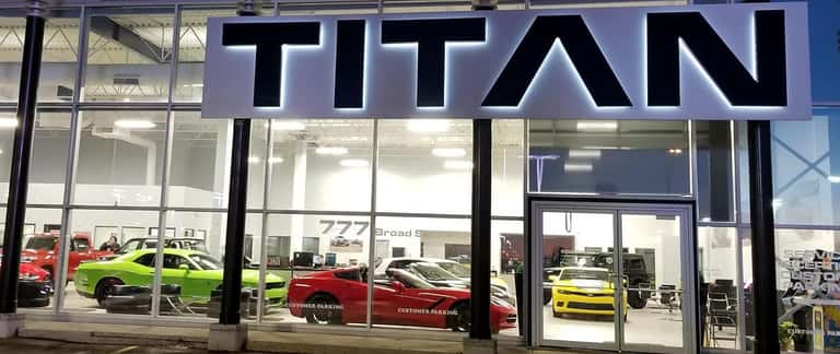 Showroom facade with illuminated "TITAN" sign, displaying vibrant sports cars inside.