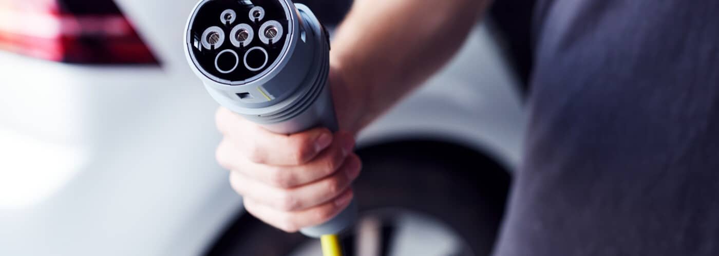 Person holding an electric vehicle charging plug near a car, highlighting eco-friendly transportation.