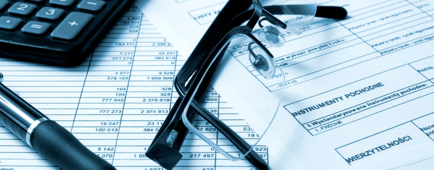 Calculator, pen, and glasses on financial documents with tables and text, emphasizing calculations.