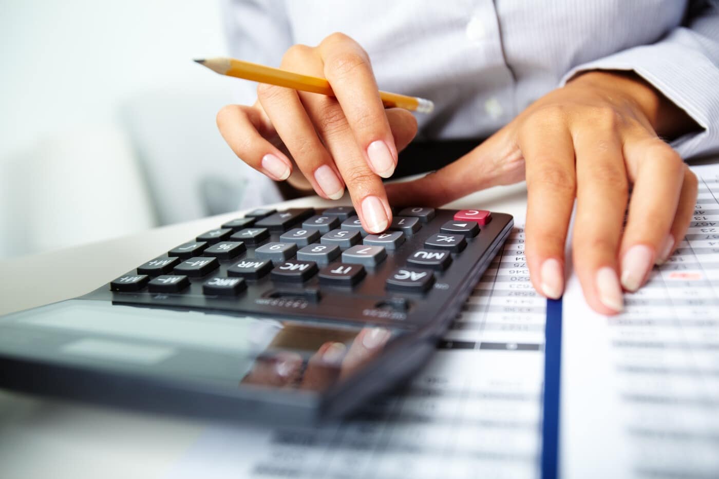 Person calculating expenses with a calculator and spreadsheet, holding a pencil.