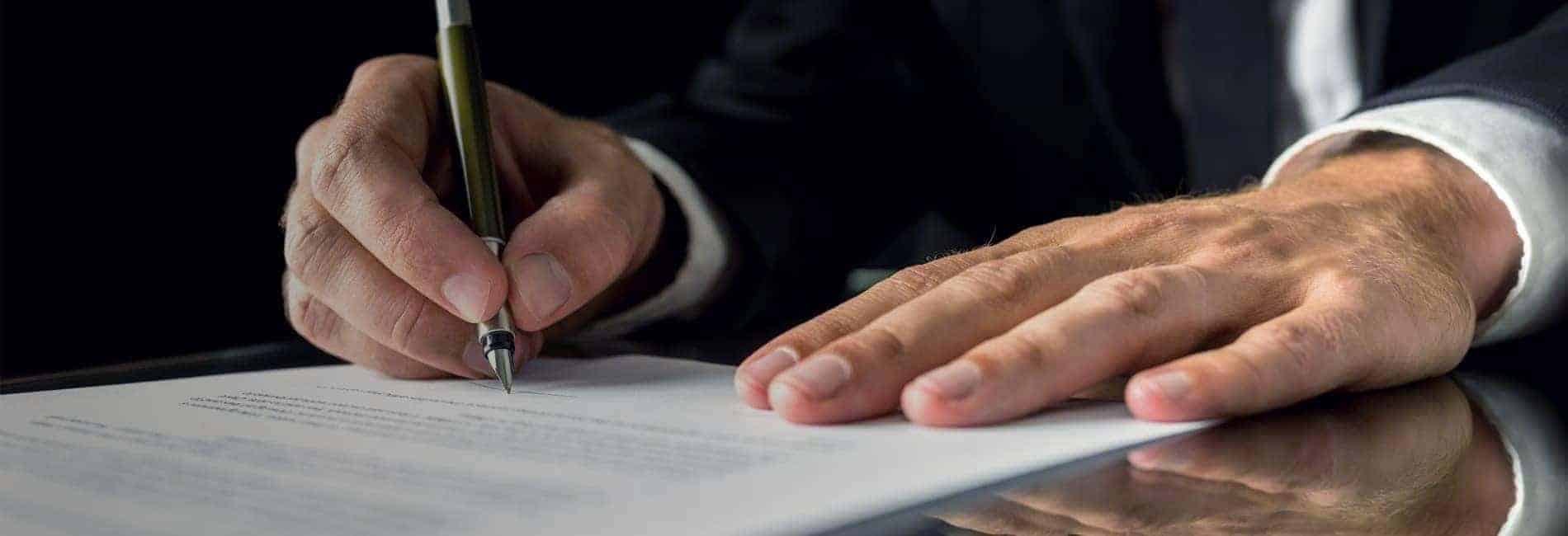 Person signing a contract with a pen on a desk, formal business attire, reflecting professionalism.