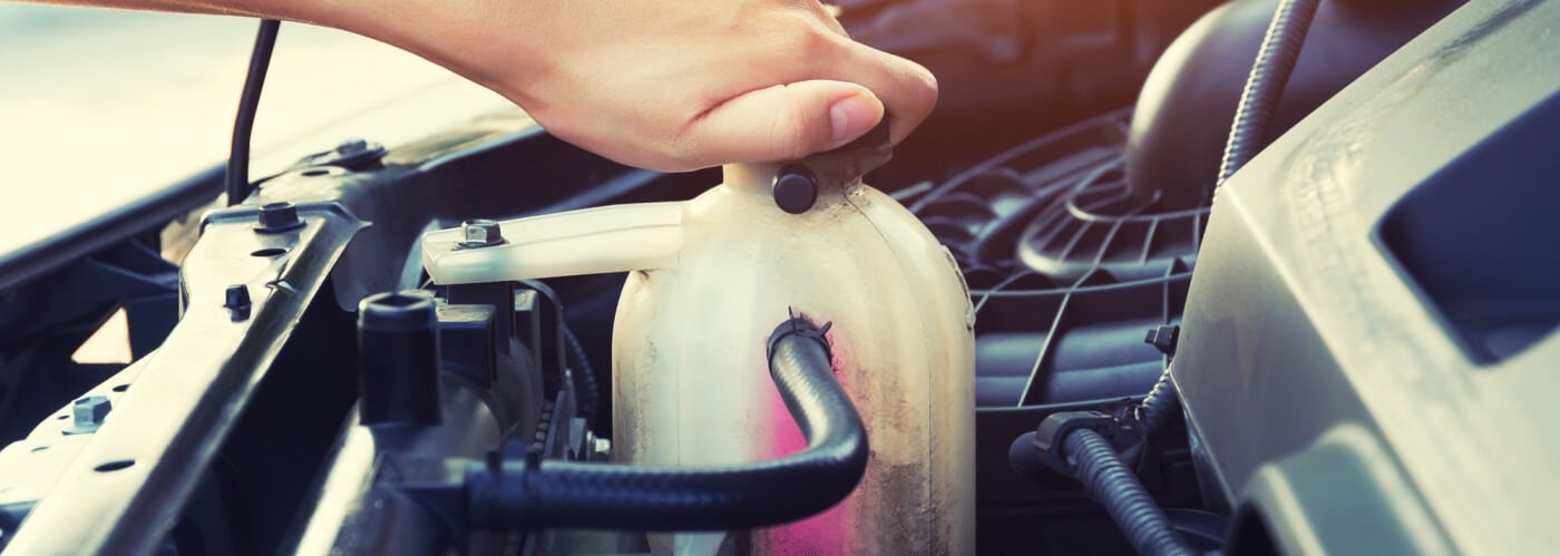 Hand opening a car coolant reservoir cap under the hood, emphasizing vehicle maintenance.