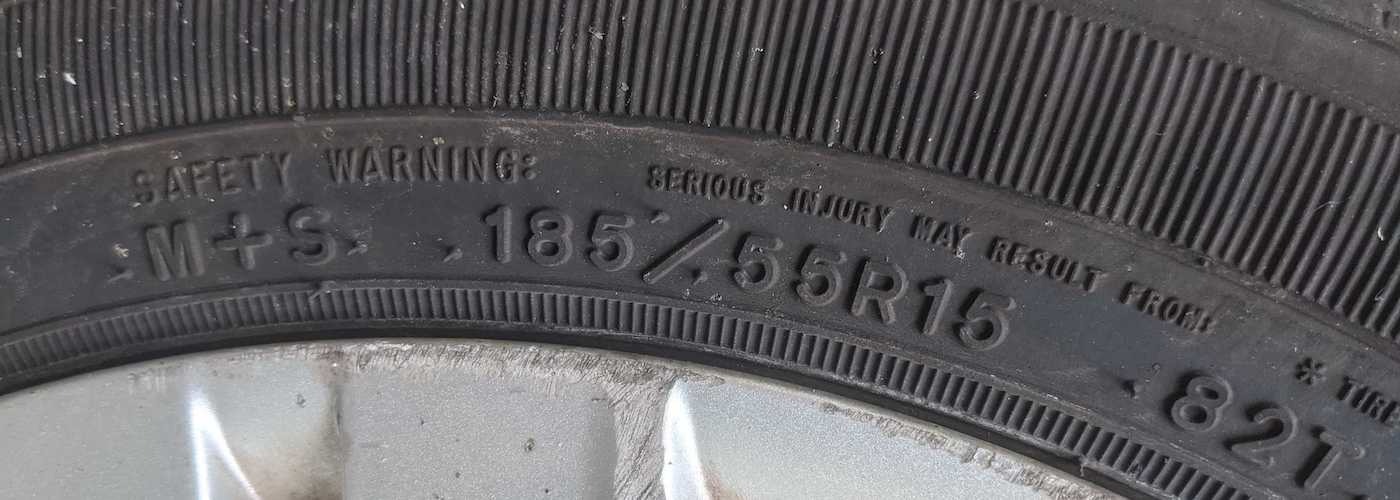 Close-up of a tire with markings M+S, 185/55R15, indicating size and type.