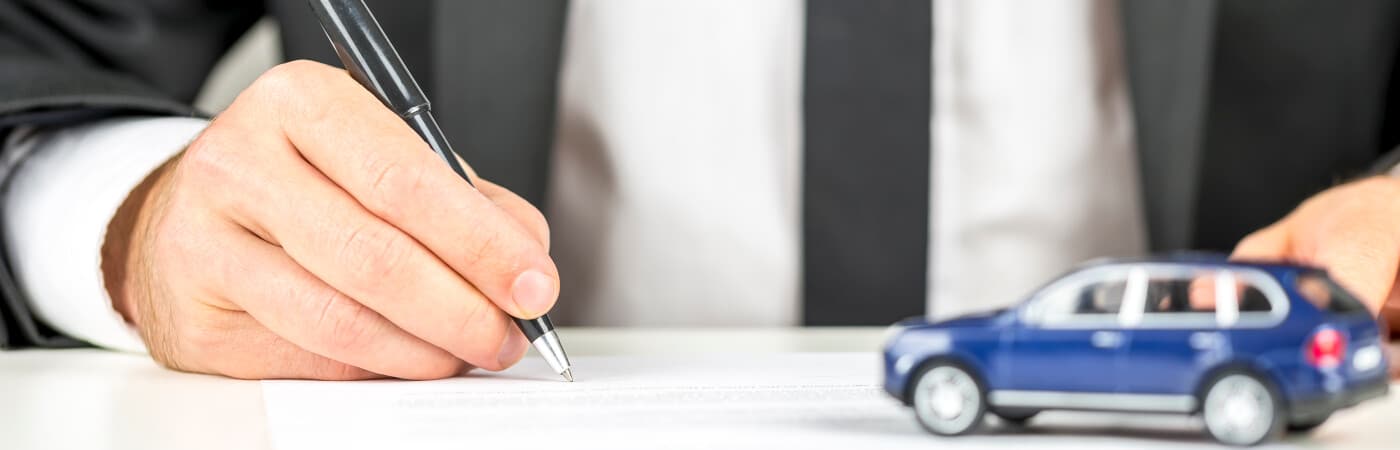 Person signing a document next to a small blue car model, symbolizing car purchase.