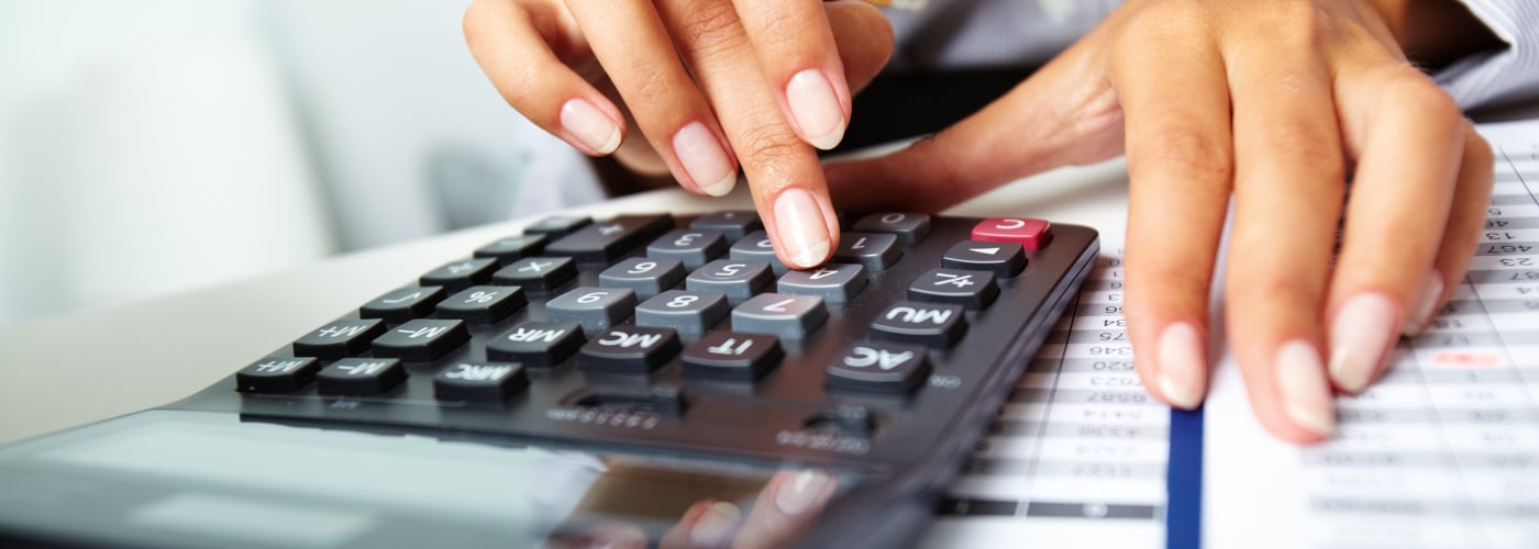 Hands using a calculator on financial documents, illustrating accounting or budgeting tasks.
