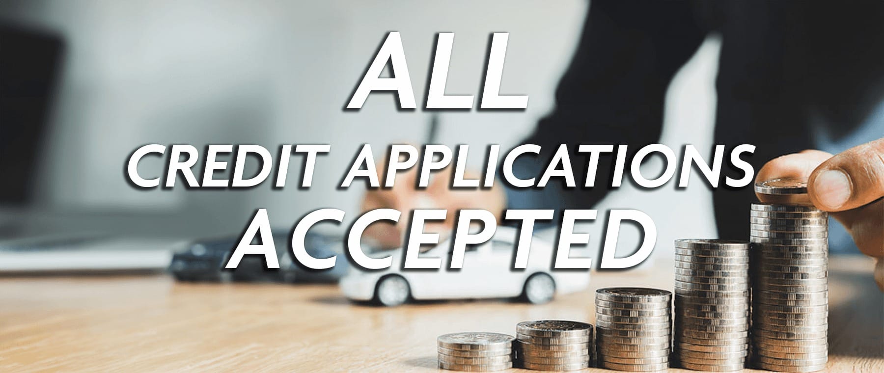 Text "All Credit Applications Accepted" over hands stacking coins and a toy car.