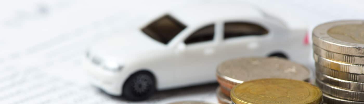 Blurred white car model with stacked coins in foreground, symbolizing car finance.