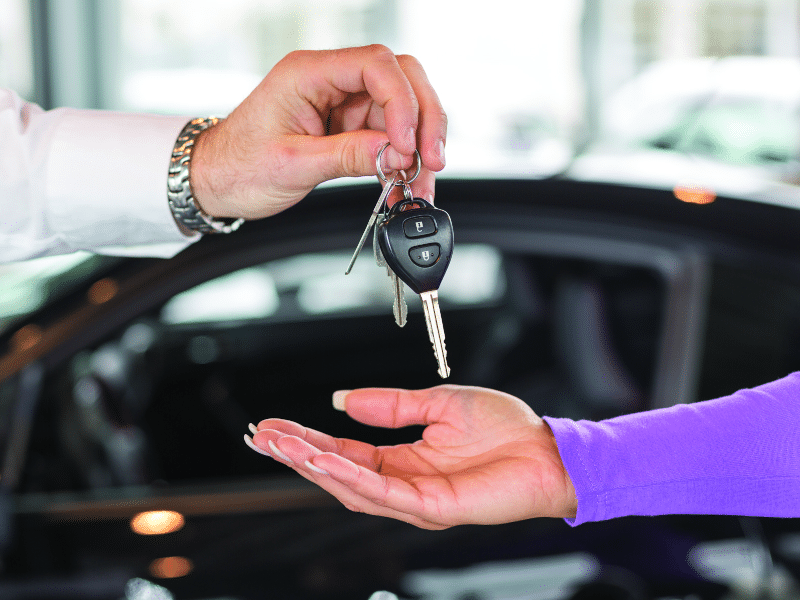 Handing over car keys in a dealership setting. Close-up of two hands exchanging keys.