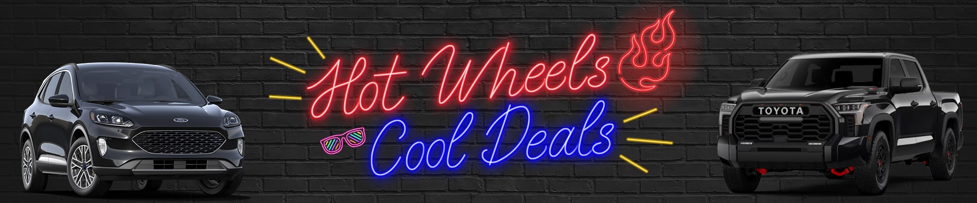 Ford SUV and Toyota truck flank neon sign saying "Hot Wheels, Cool Deals" on a brick wall.
