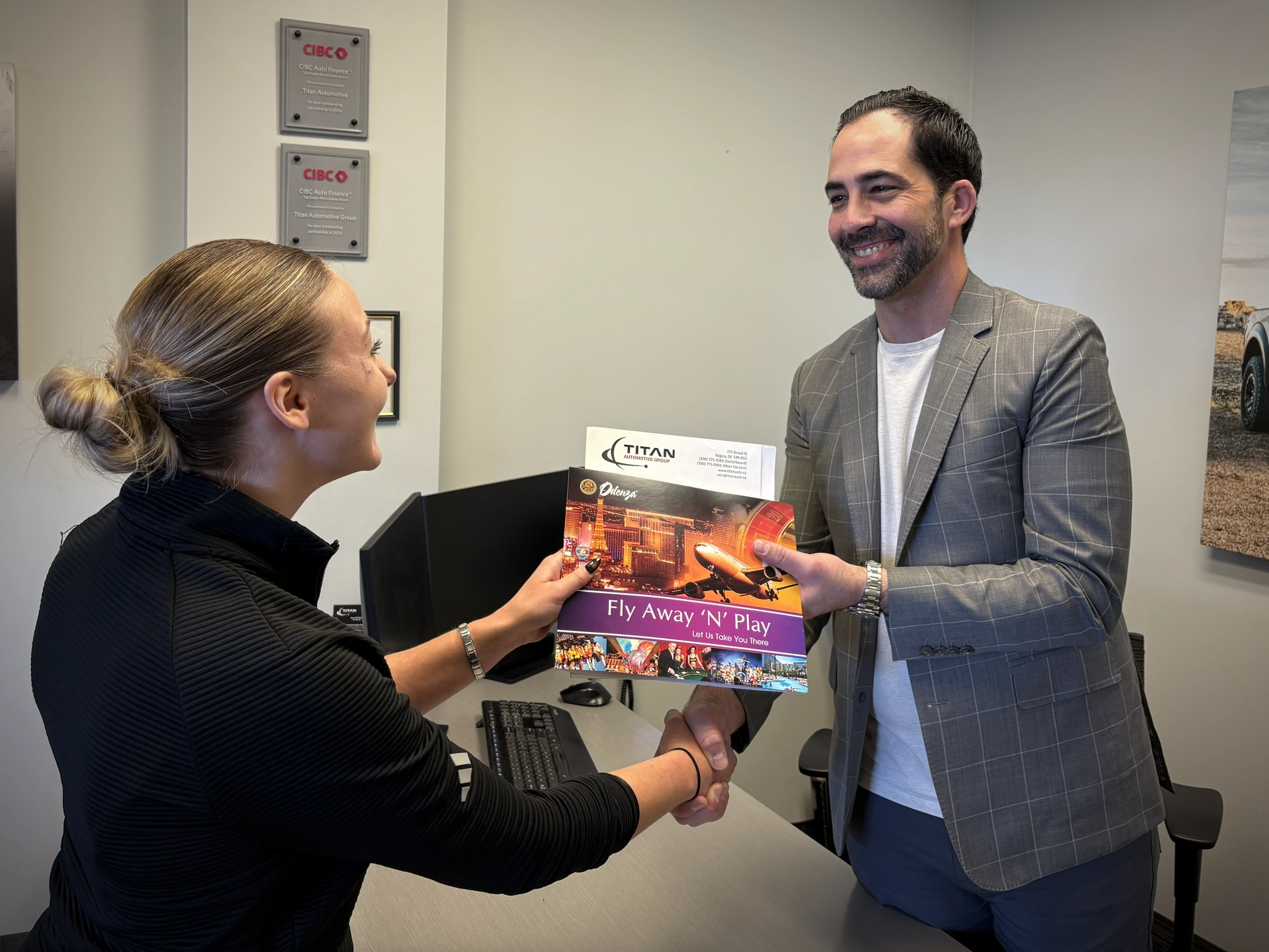 Two people exchanging a travel brochure titled "Fly Away 'N' Play" in an office setting.