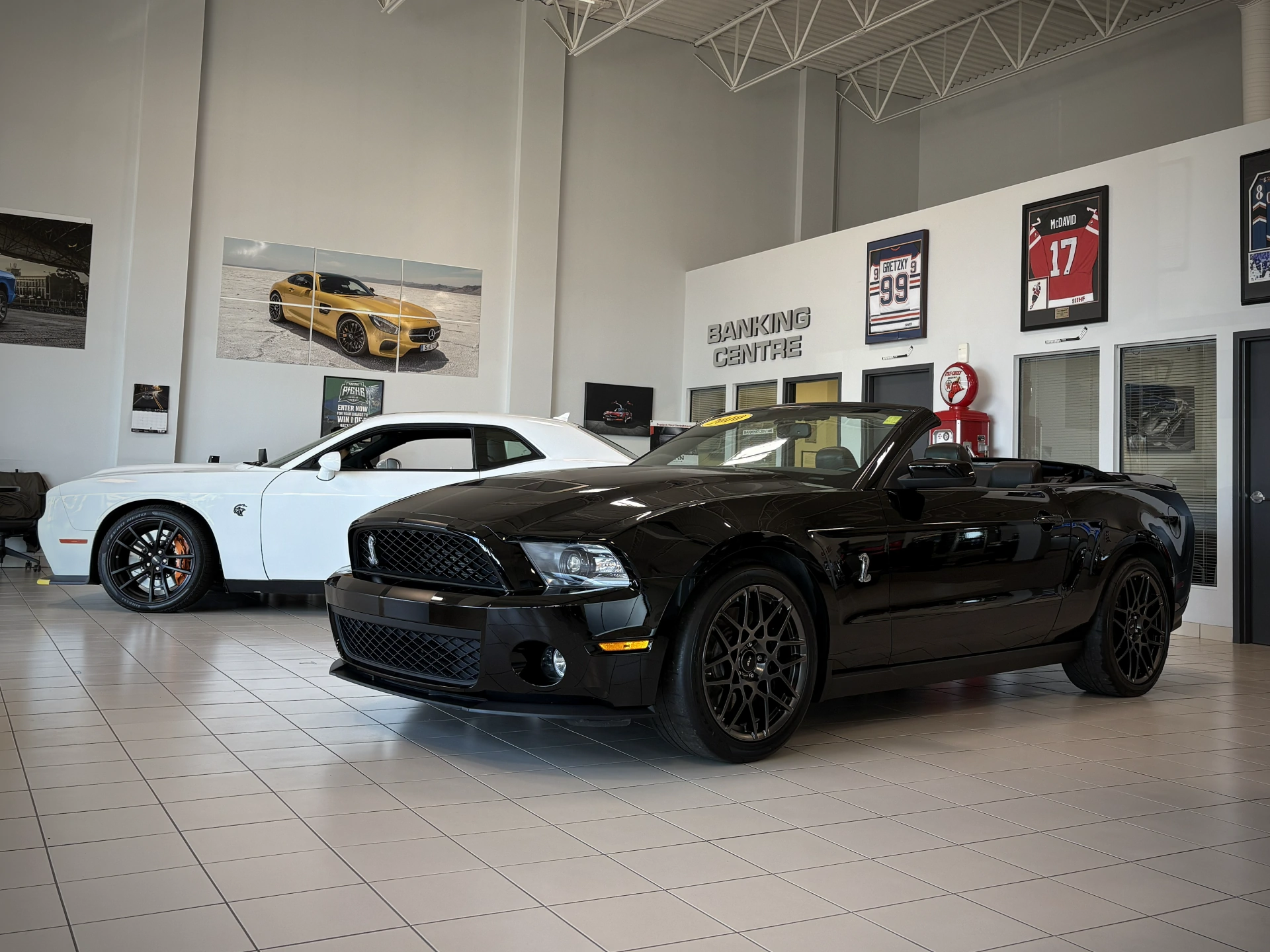 Black convertible and white sports car displayed in an automotive showroom with sports memorabilia.