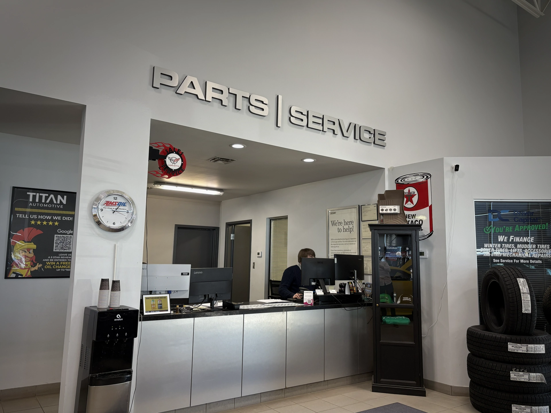 Auto parts and service desk with employee, promotional posters, and stacked tires in a showroom.